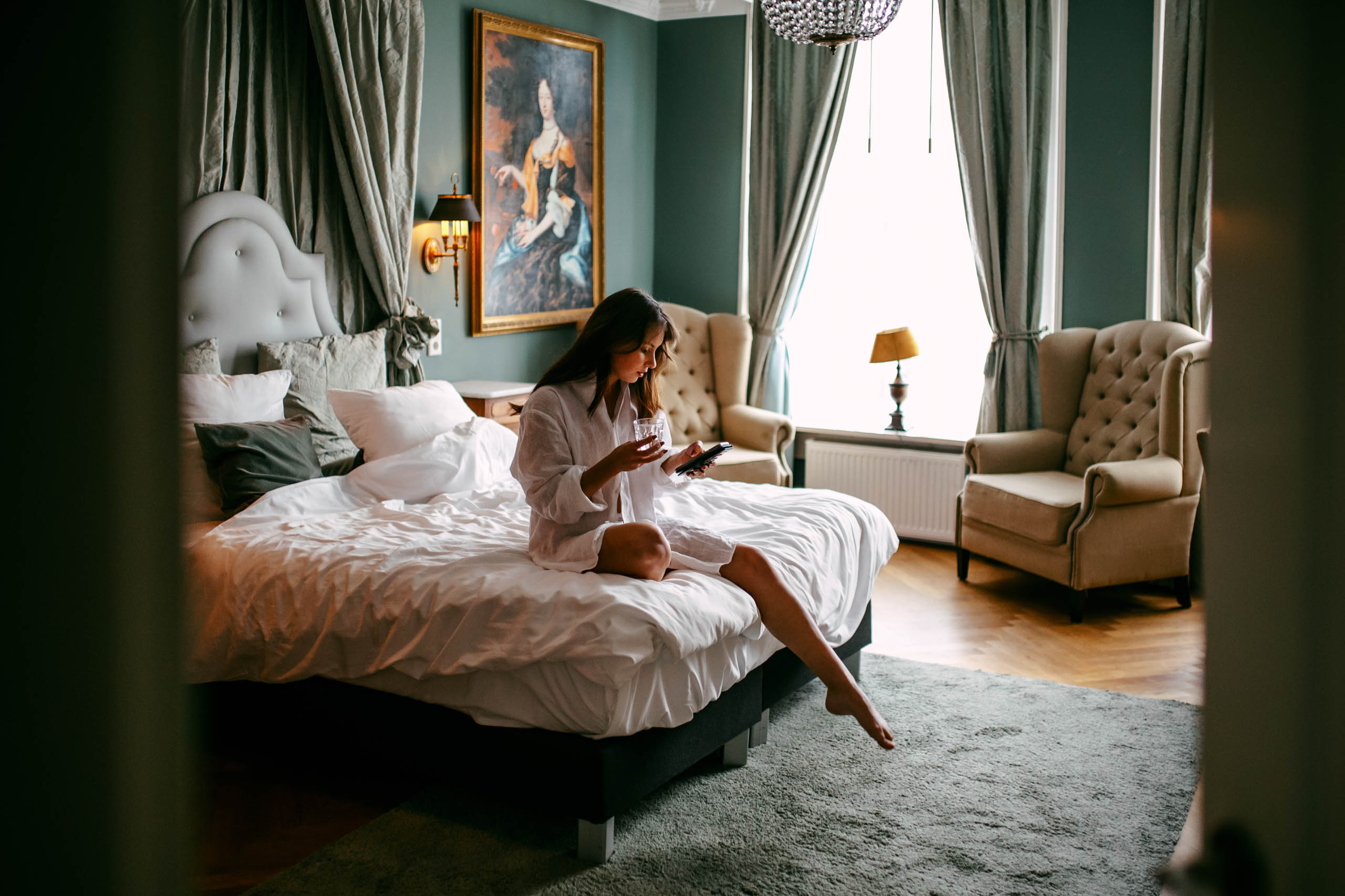 Een boudoir-geïnspireerde vrouw zittend op een bed in een hotelkamer.