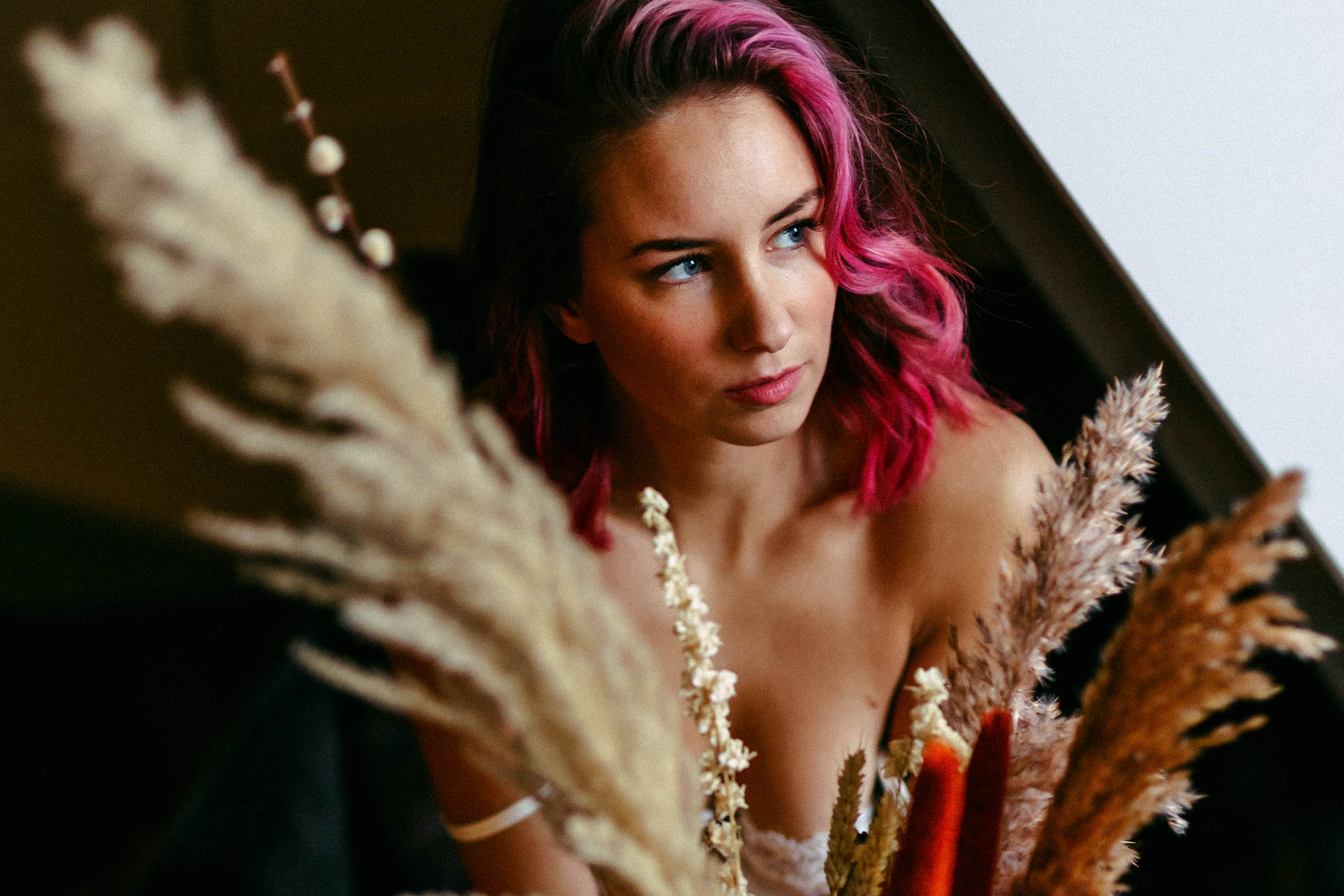 A woman with pink hair poses in front of a window and shows tips for boudoir photography.