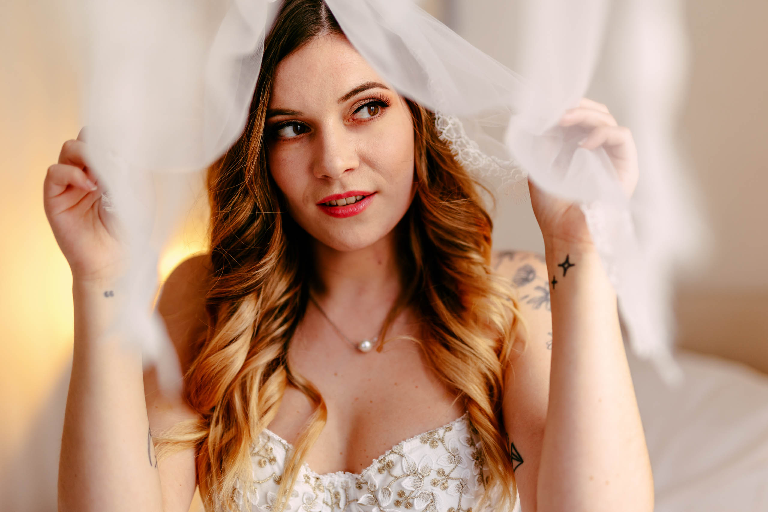 A beautiful bride in a white wedding dress, gracefully posing for a boudoir shoot in The Hague, with a delicate veil elegantly covering her head.