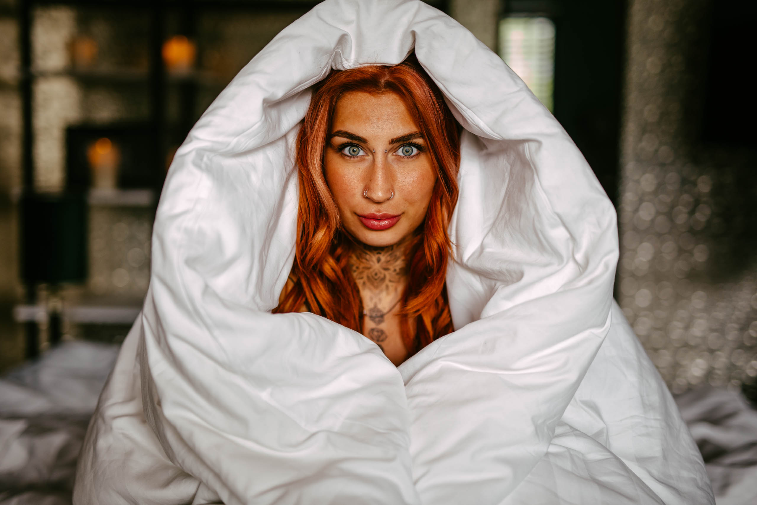 Een vrouw met rood haar, gewikkeld in een deken op een bed.