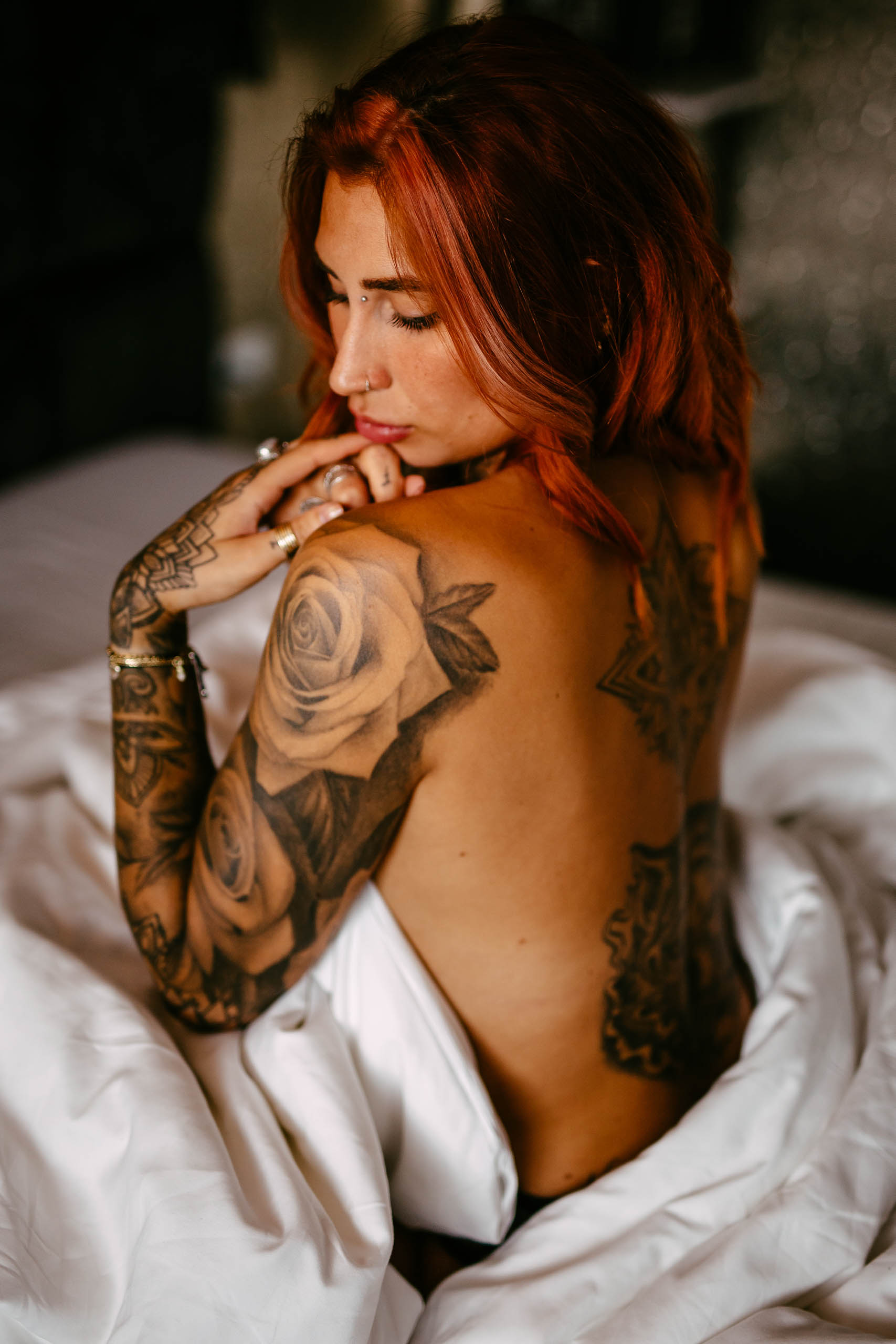 Een vrouw met rood haar en tatoeages liggend op een bed.