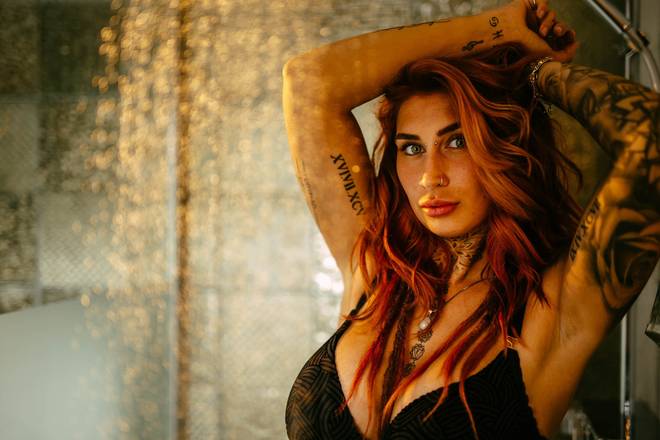 A woman with red hair and tattoos poses in the shower.