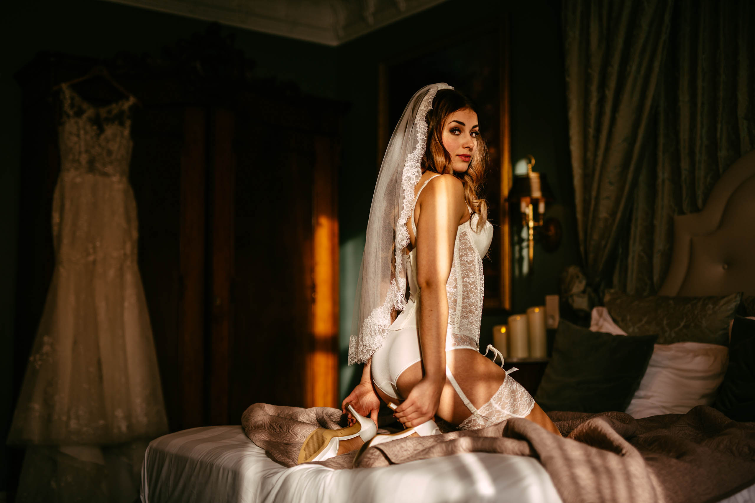 A bride in a lace dress poses on a bed during a boudoir shoot in Delft.