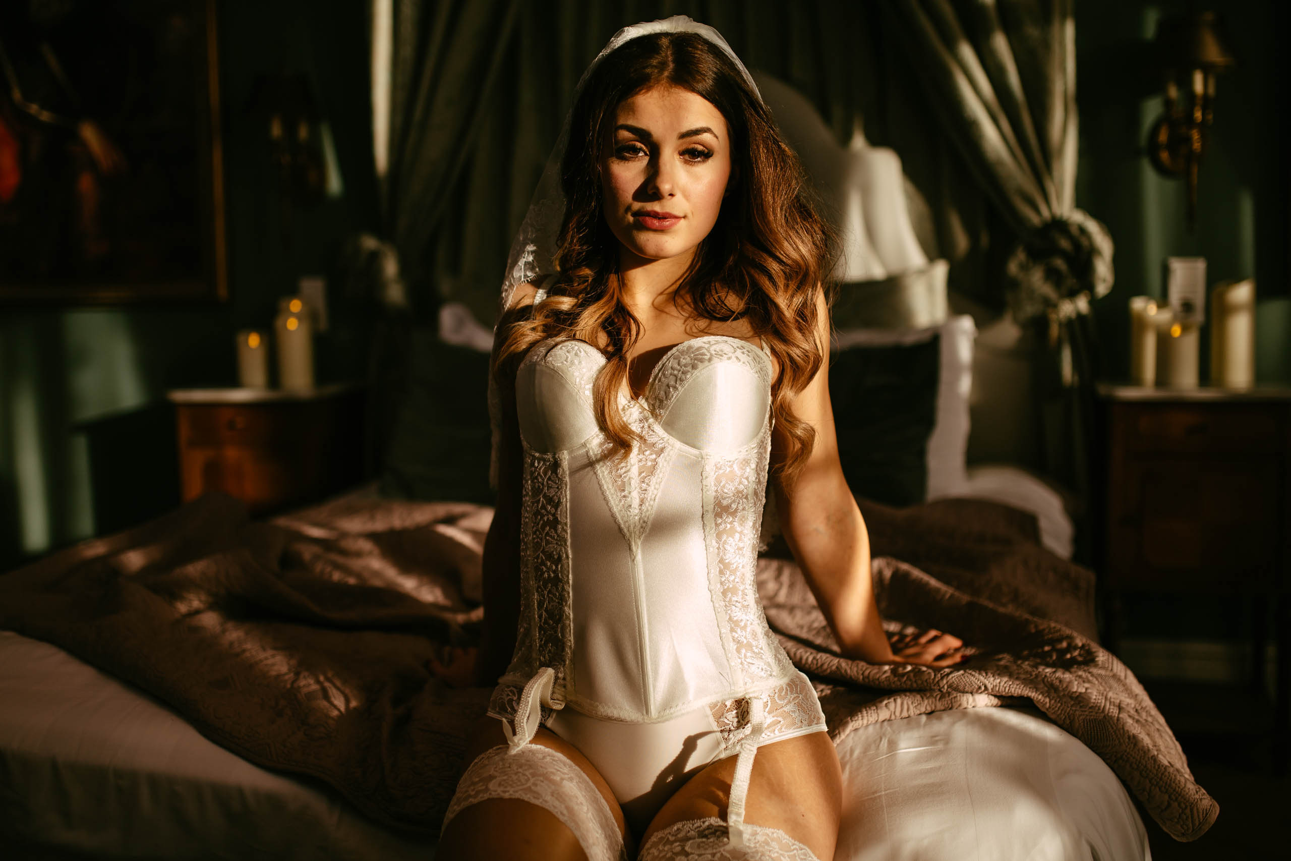 Een mooie vrouw in een wit korset zittend op een bed tijdens een boudoirshoot in Delft.