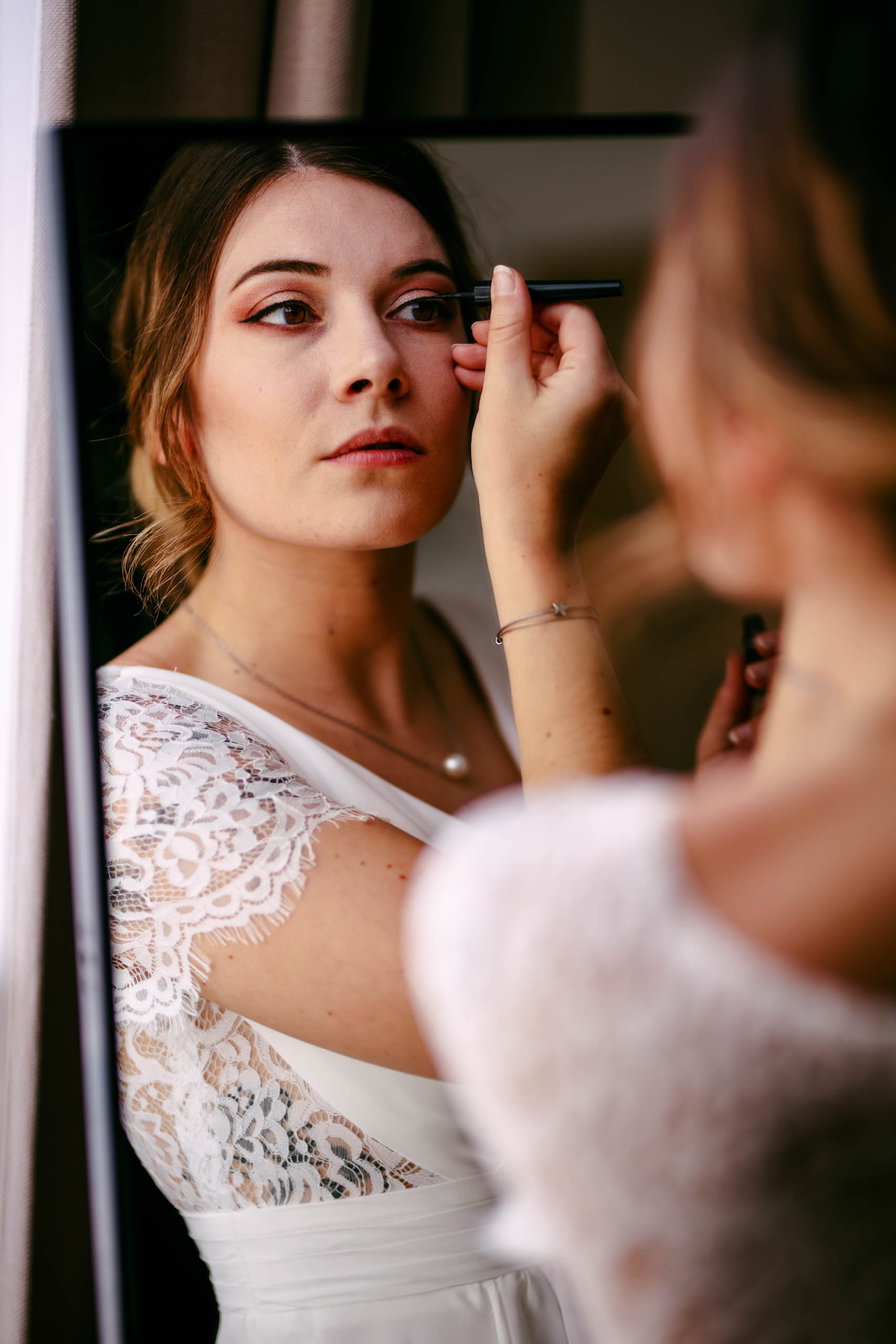 A bride gets her make-up done in front of a boudoir-shooting mirror.