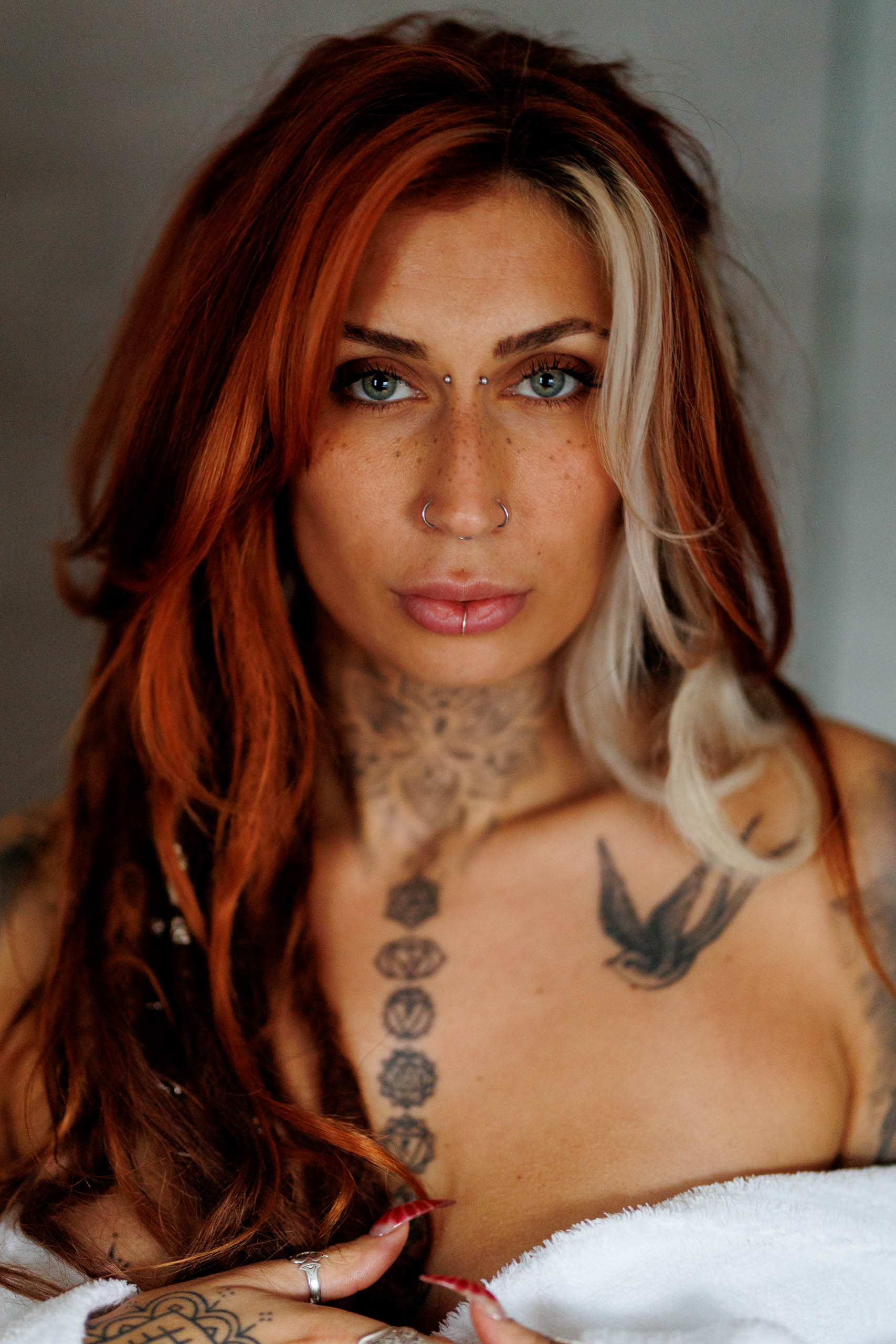 A woman with red hair and tattoos poses in a towel for a glamour photo shoot.
