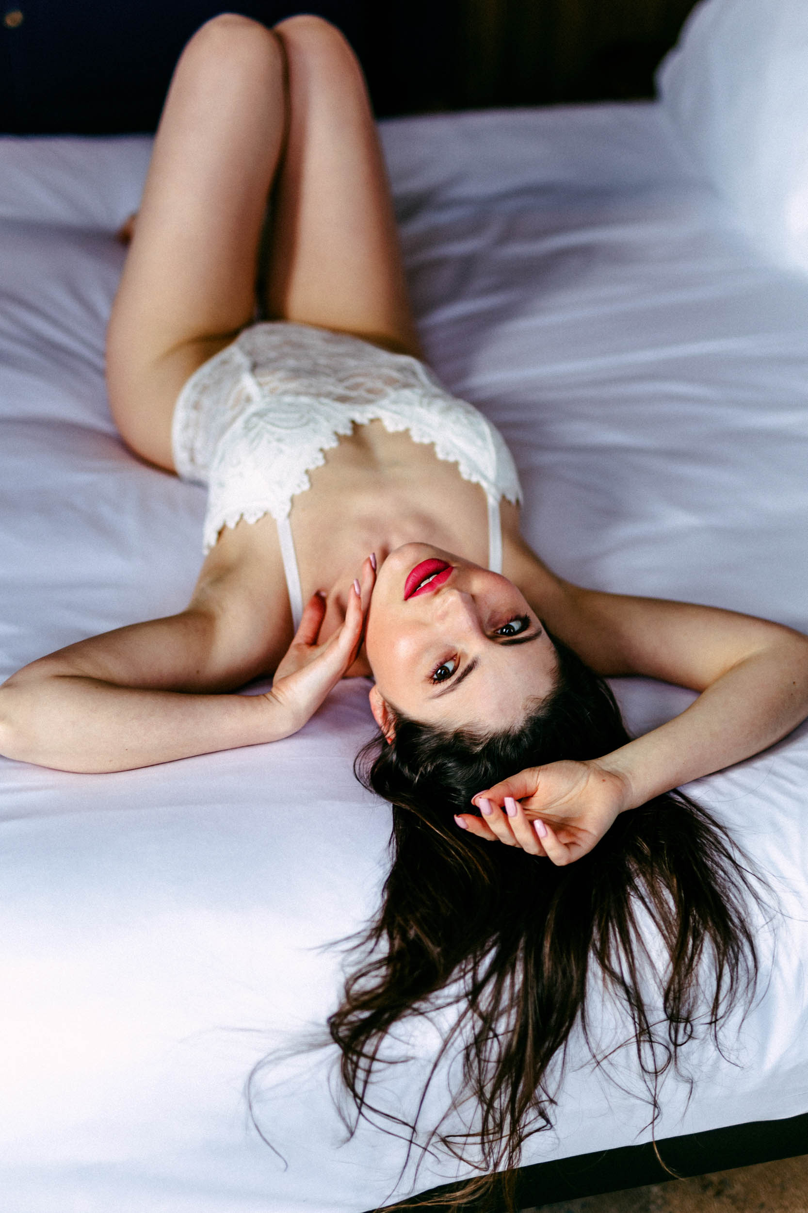 Een prachtige vrouw in Den Haag, poserend voor een boudoirfotoshoot op een smetteloos wit bed.