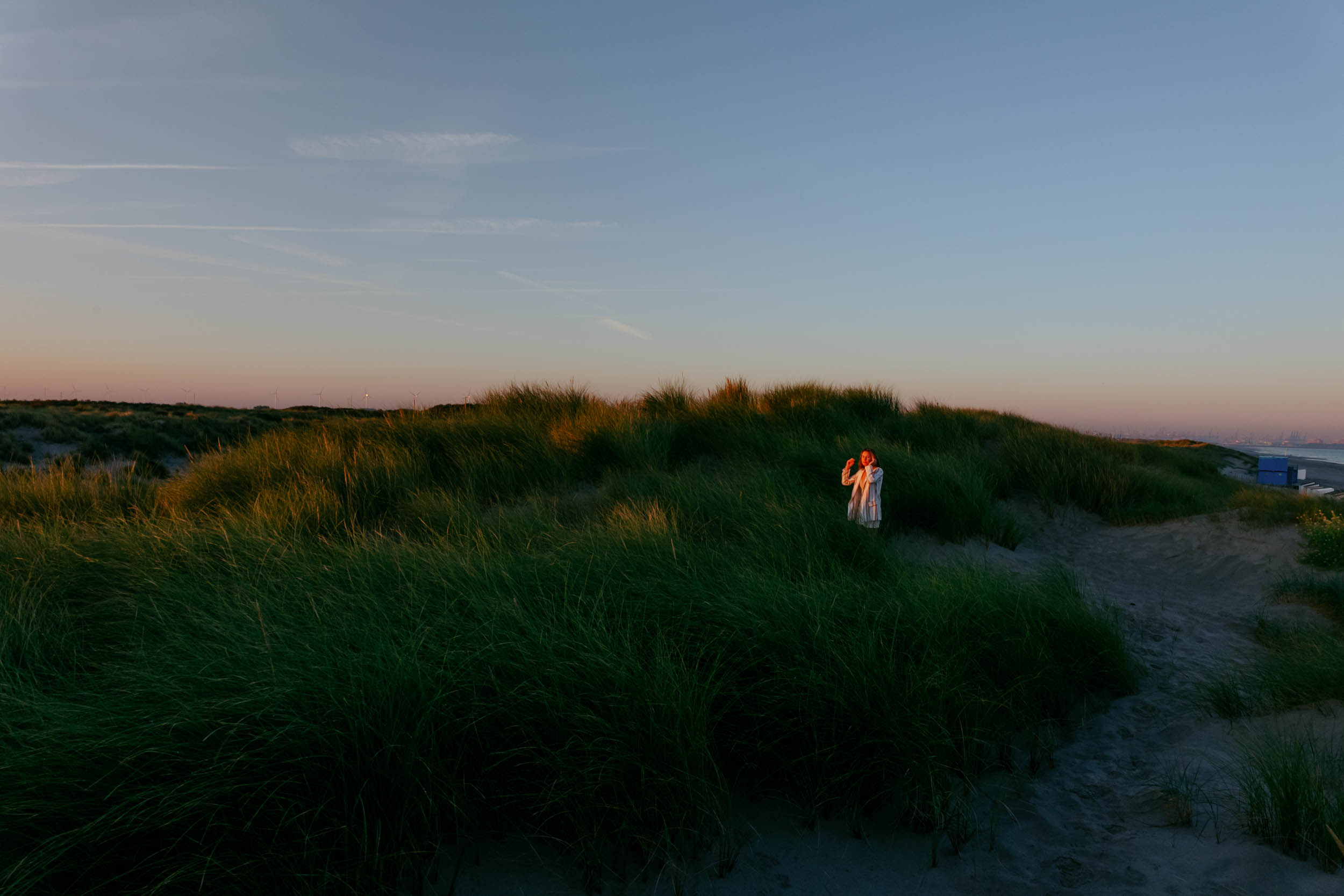 A woman poses for a photograph on a sand dune at sunset.