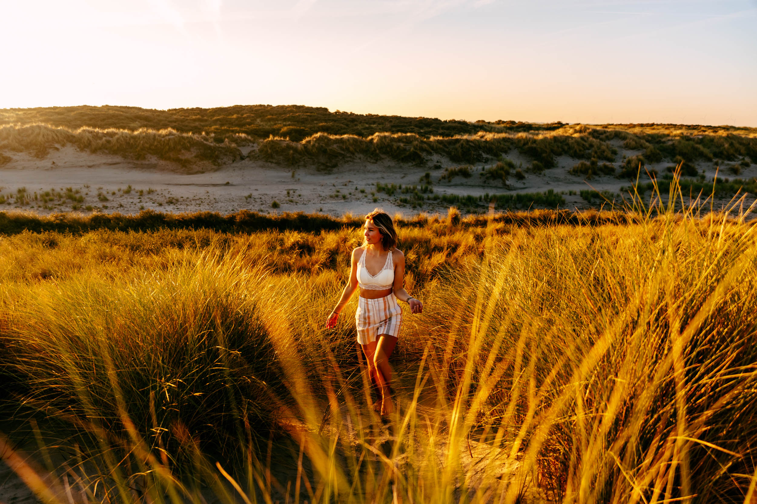 A woman strolling through tall grass at sunset, captured in beach photos.