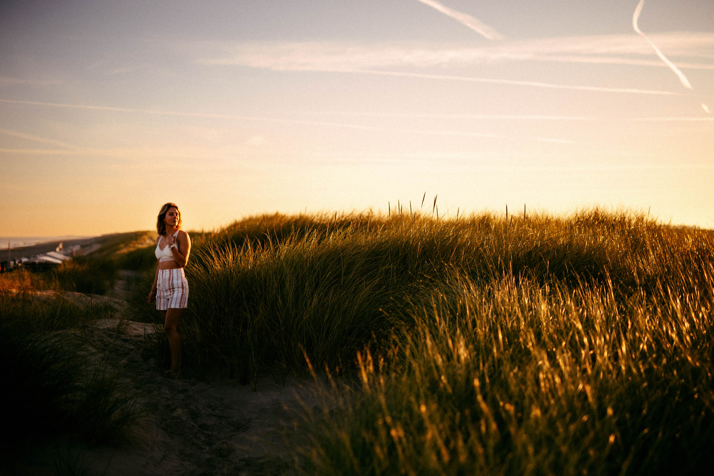 A woman standing in a field of tall grass at sunset, captured in an enchanting "beach photo".