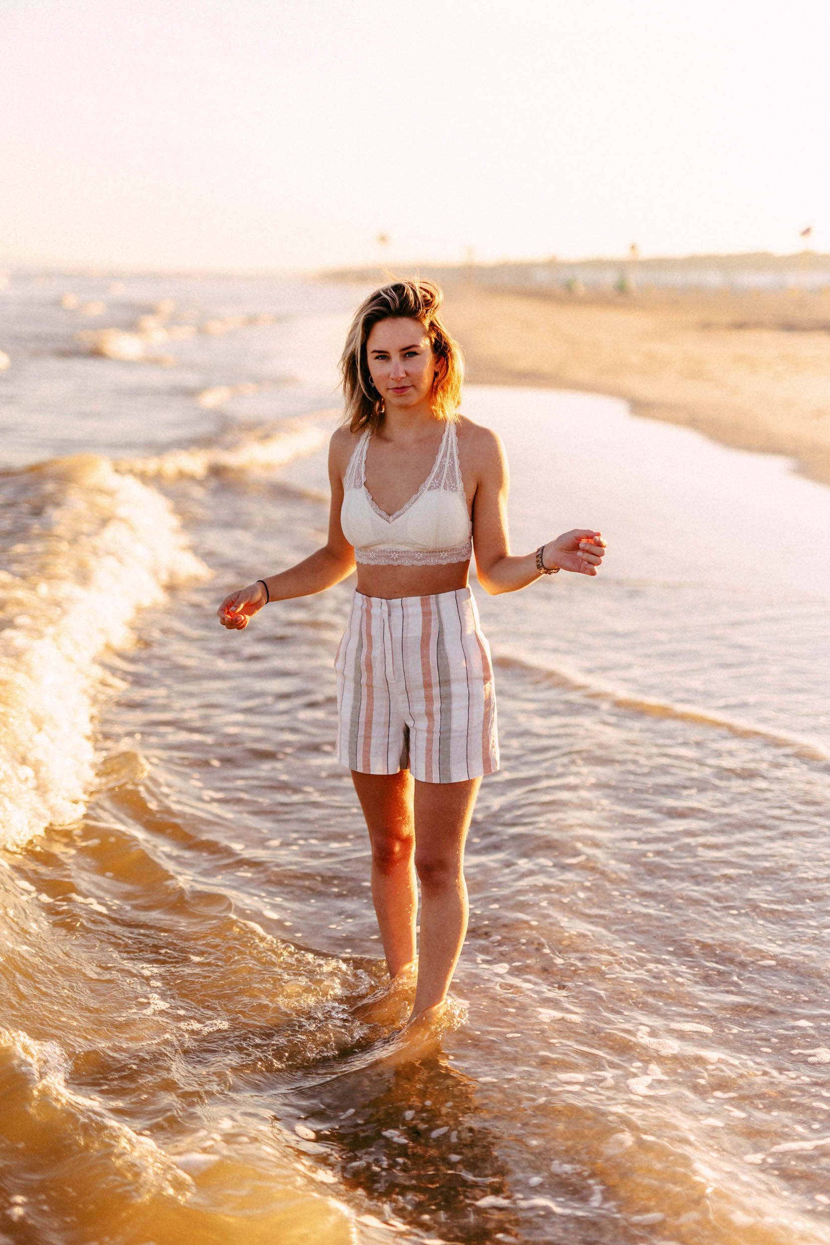 A woman standing on a beach, dressed in shorts and a striped top, captured in beautiful photographs.