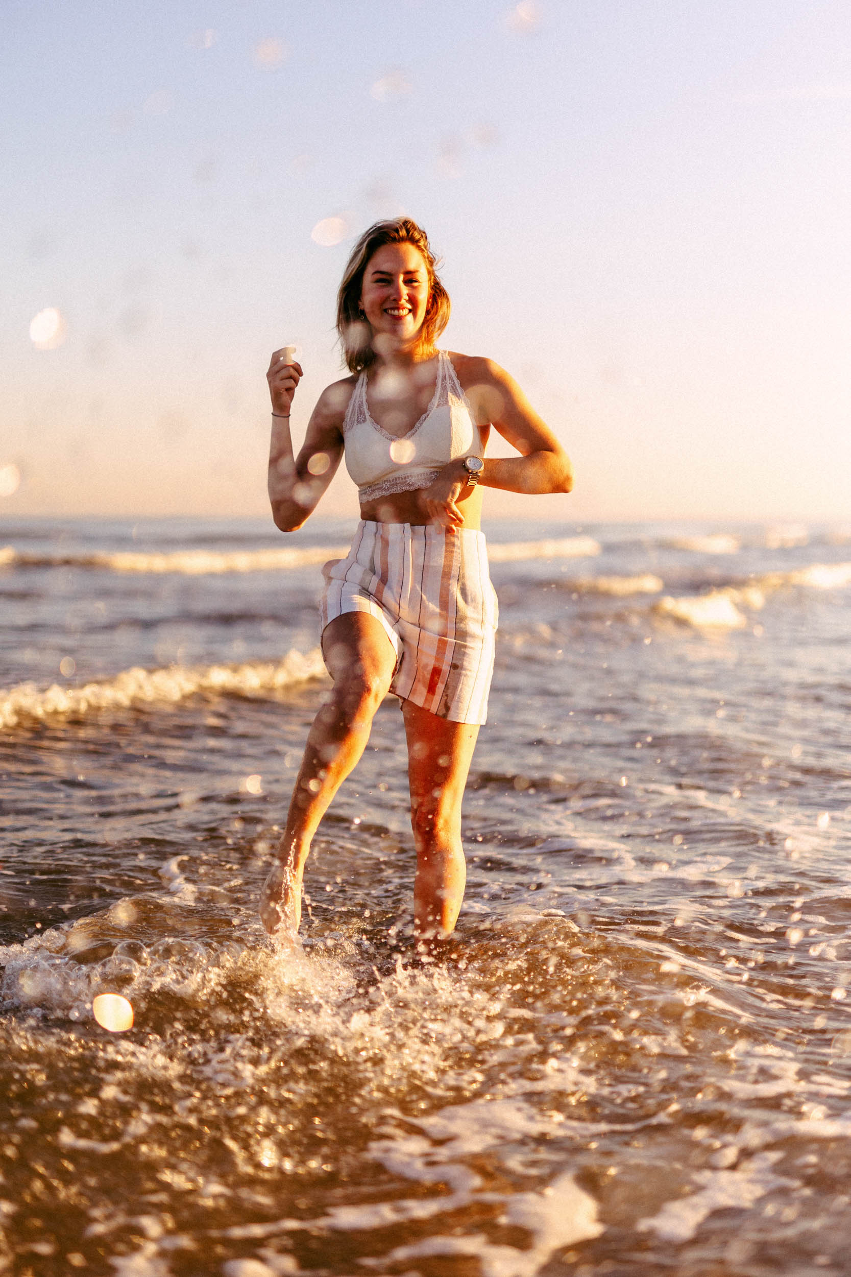 A woman poses for beach photos while running in the ocean at sunset.