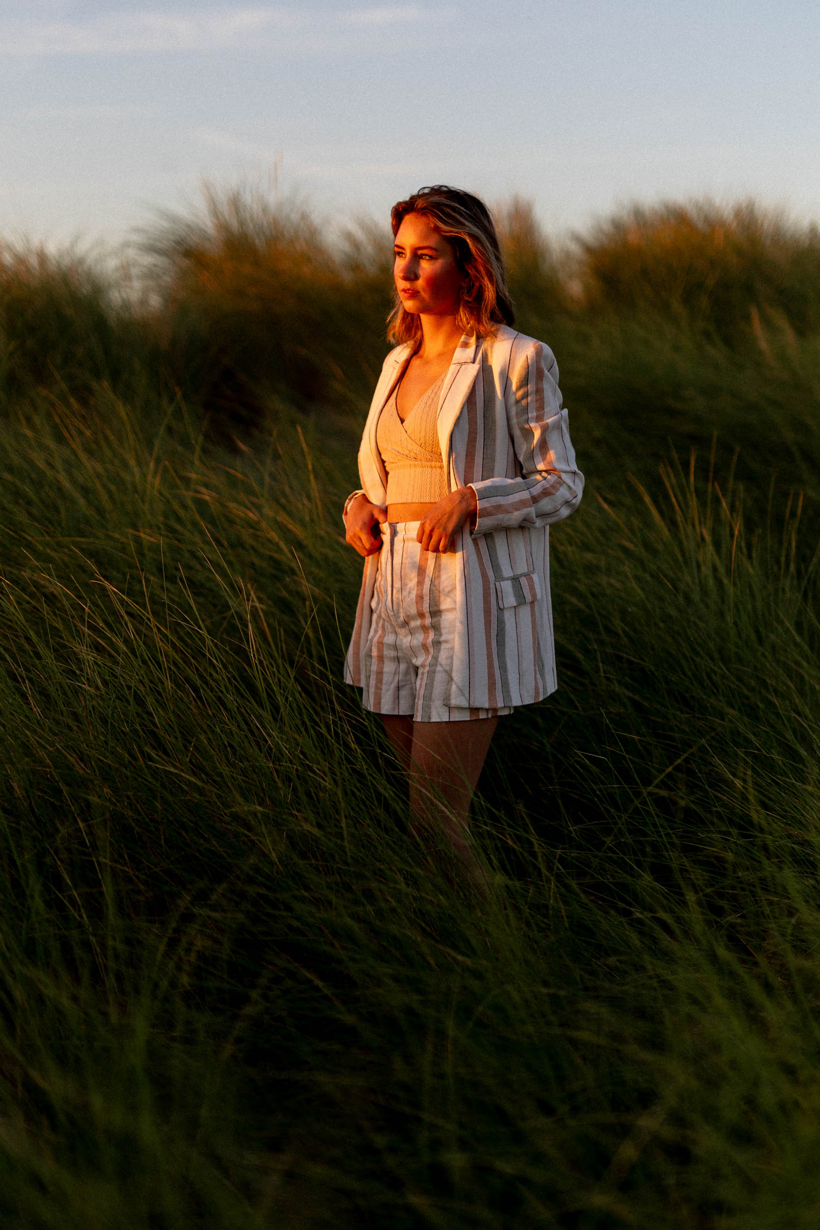 A woman in a blazer and shorts taking beach photos in tall grass.