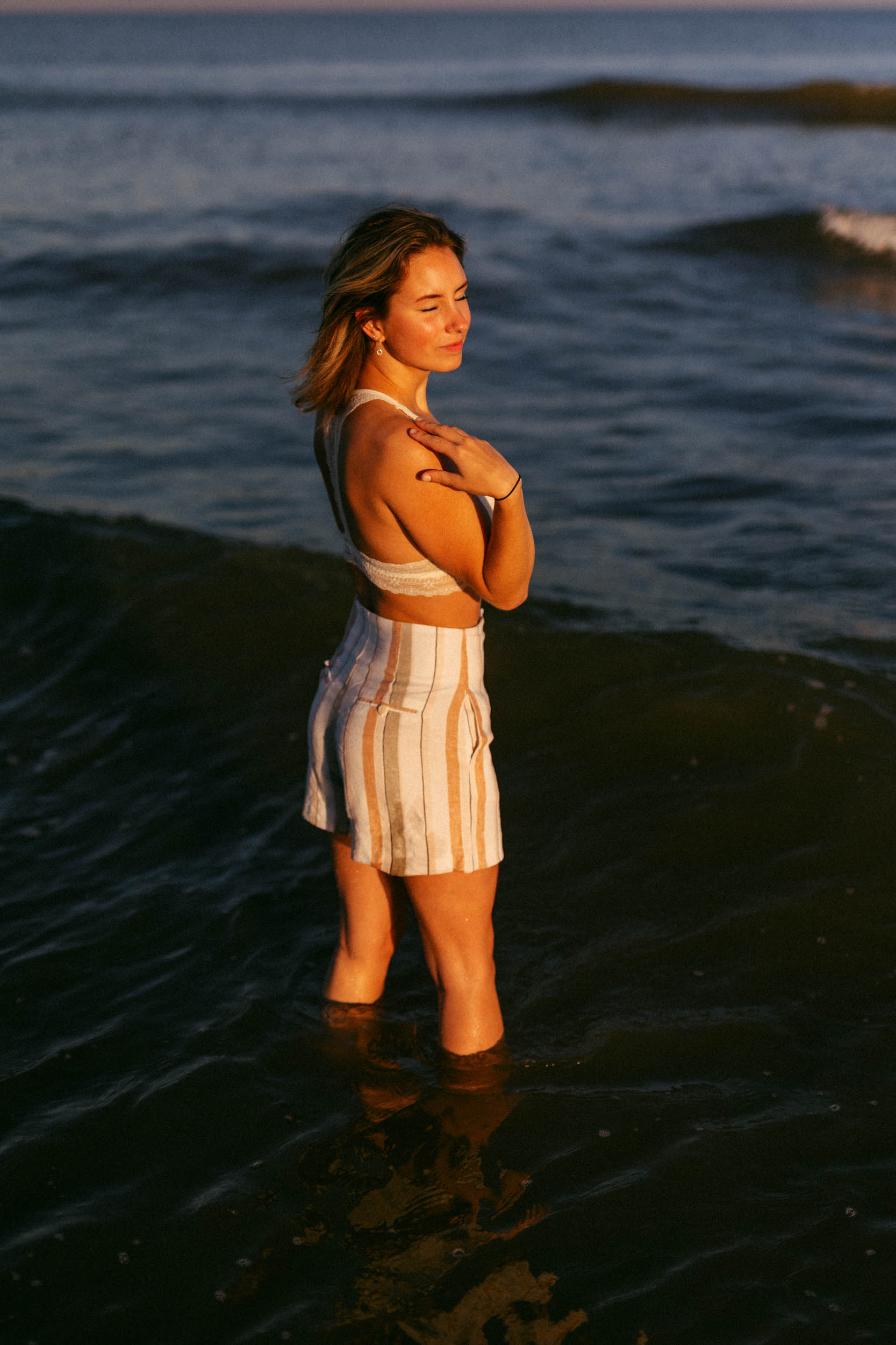 A woman standing in the ocean, dressed in a striped top and shorts, captured in a beautiful beach photo.