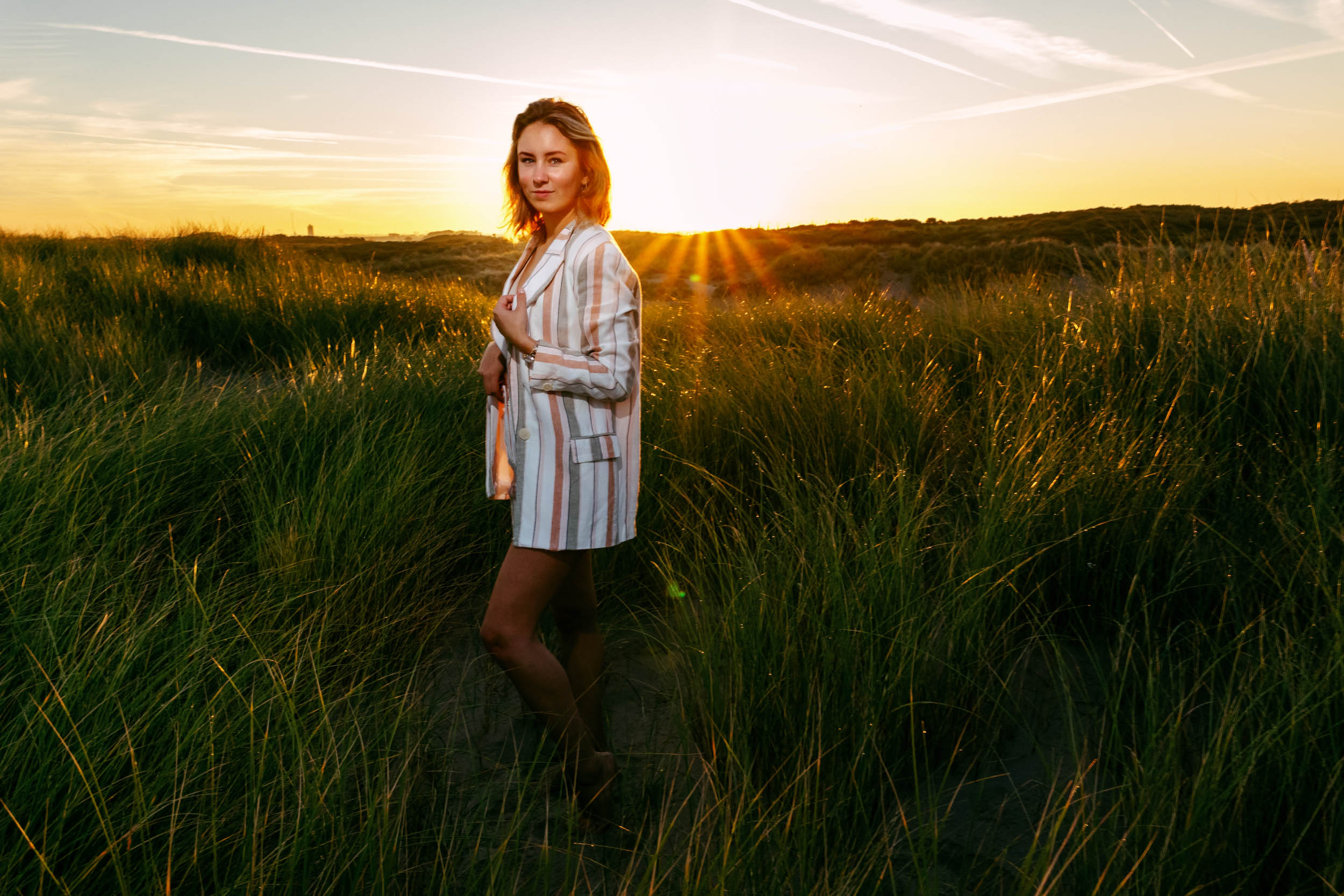 A woman in a striped dress standing in tall grass at sunset.