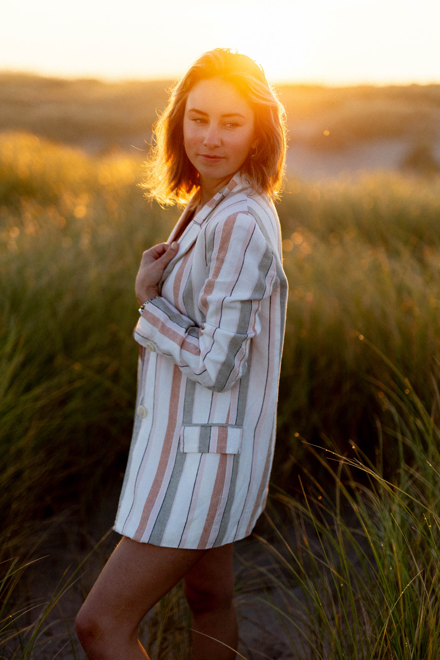 A woman in a striped blazer poses for beach photos in tall grass.