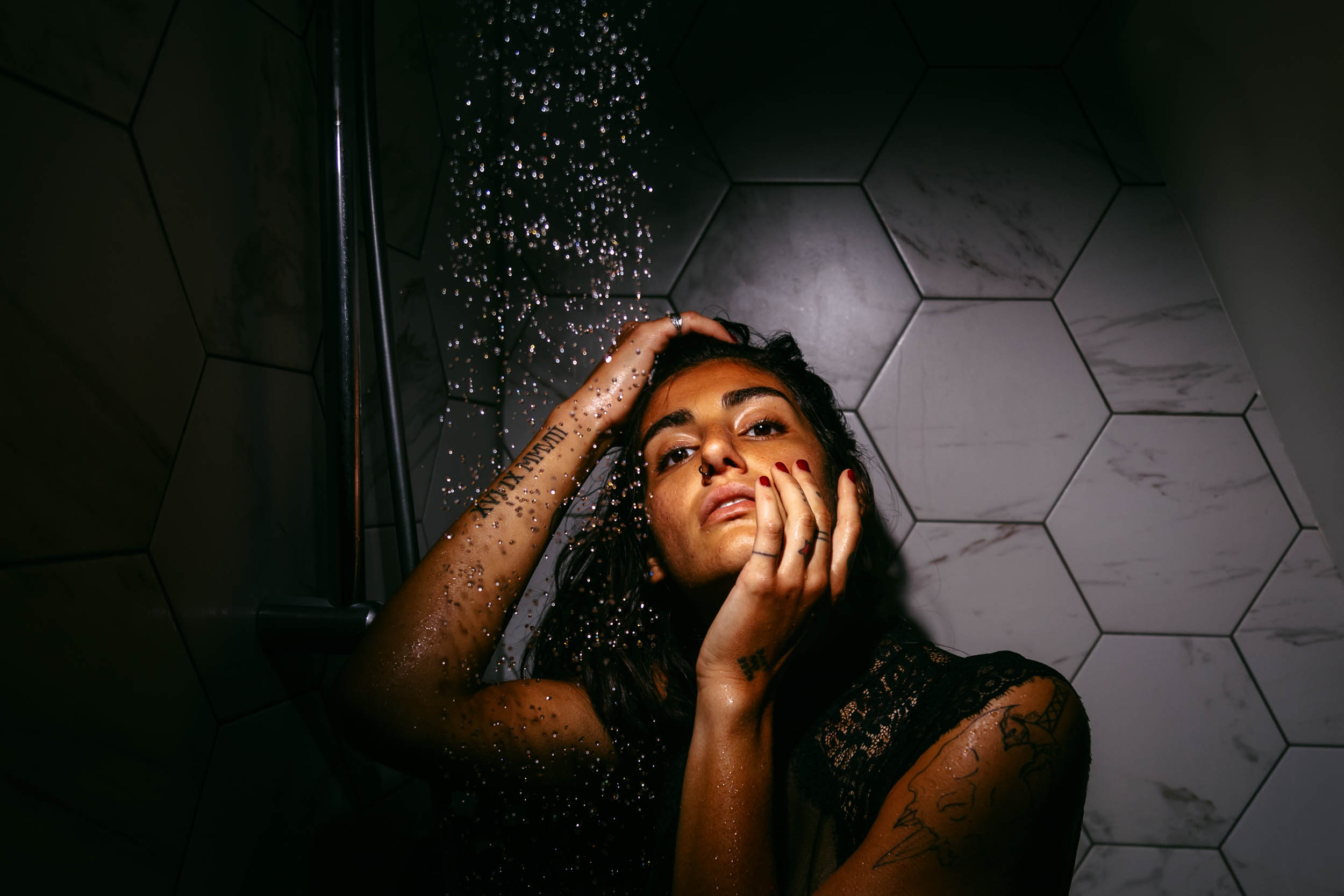 A woman stands under a shower during a beach photo shoot, with her hand on her face.