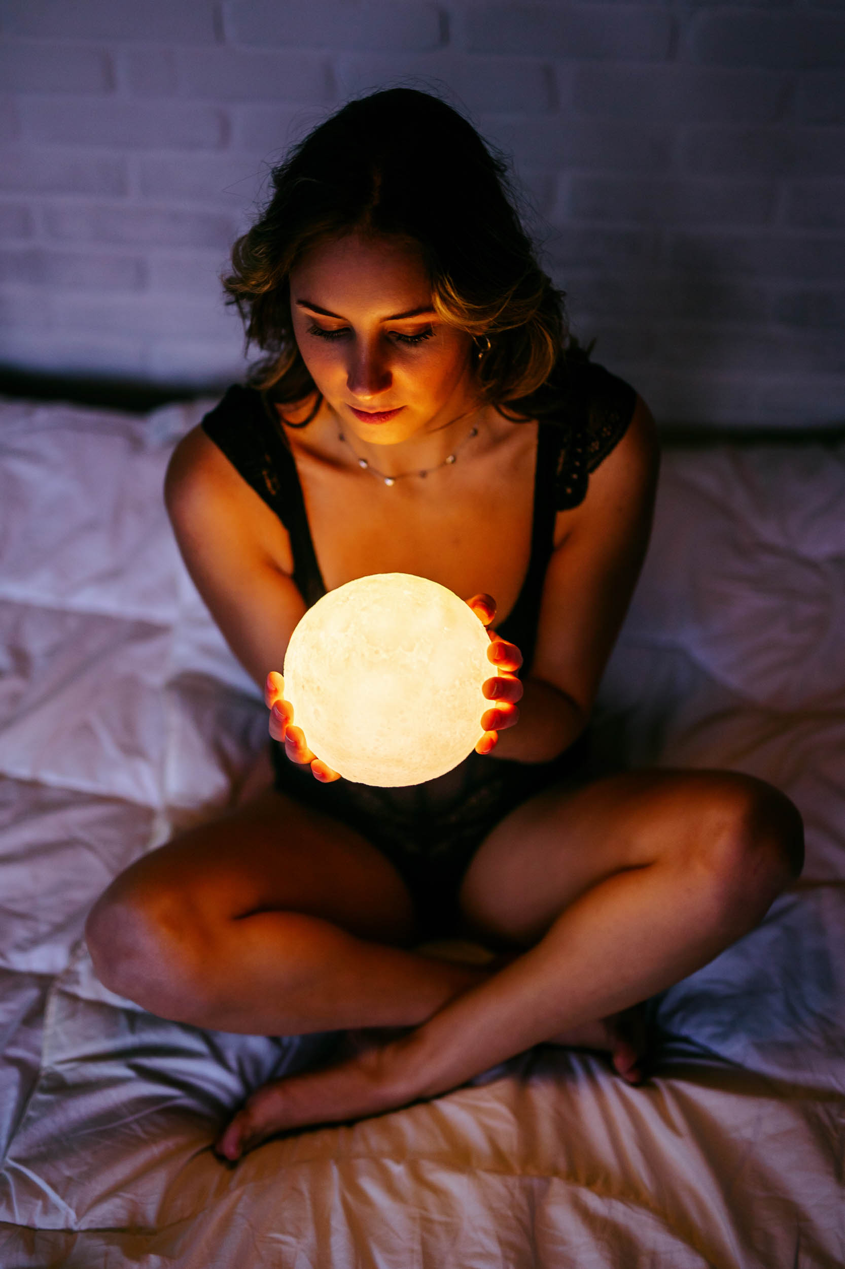 A woman sits on a bed and holds a moon.