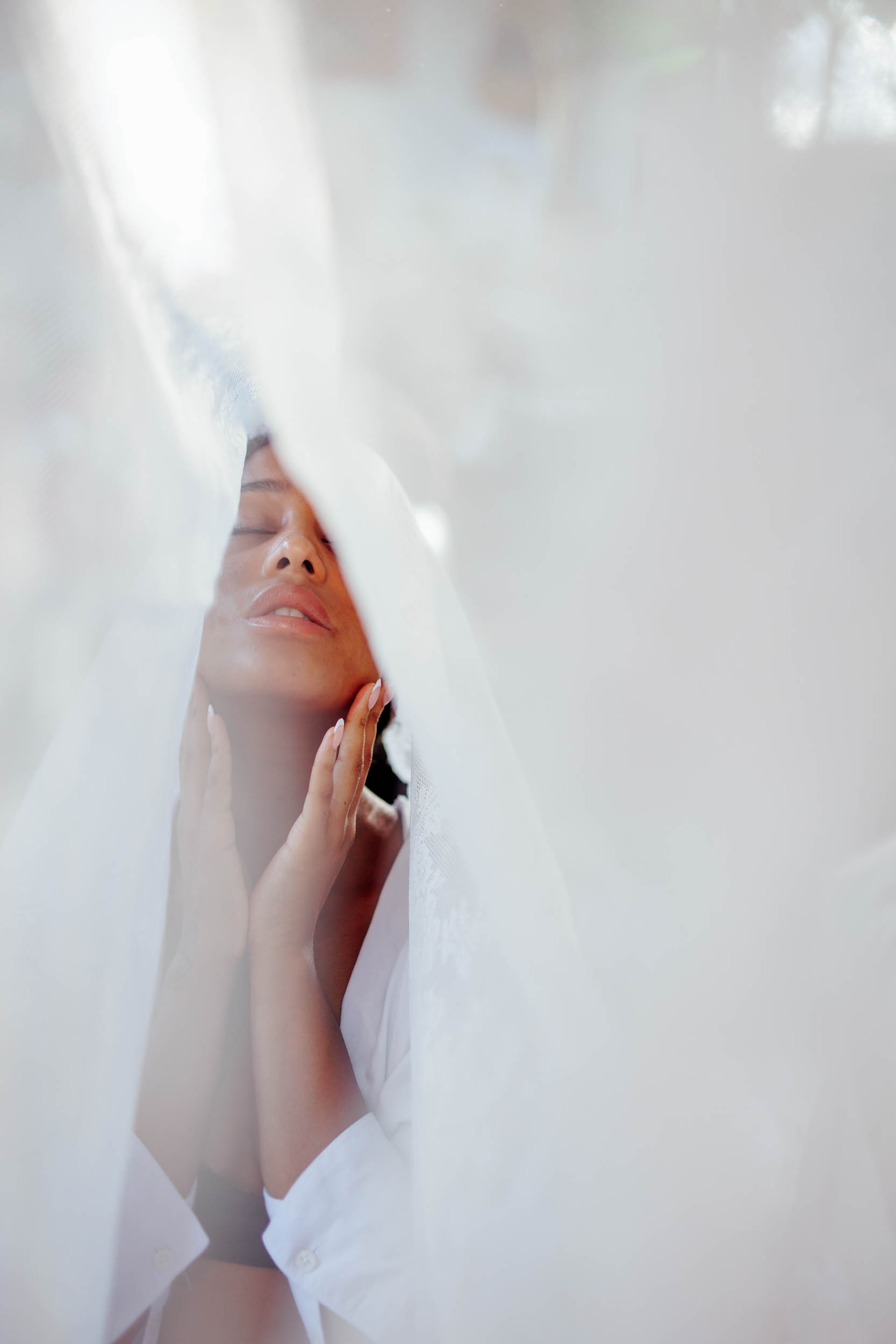 A person with closed eyes touches his face with both hands, partially covered by a white fabric.