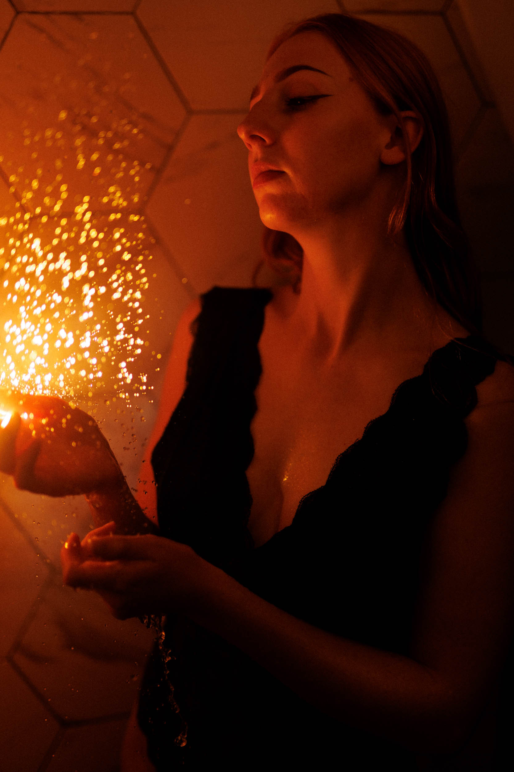 A woman holds a star in the twilight, causing a warm orange light and reflections to appear on the tiled wall behind her.